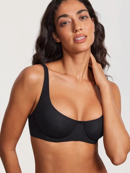 Model wearing a black full-cup bra with broad shoulder straps, smooth molded cups, and a wide supportive underband in a neutral studio setting.