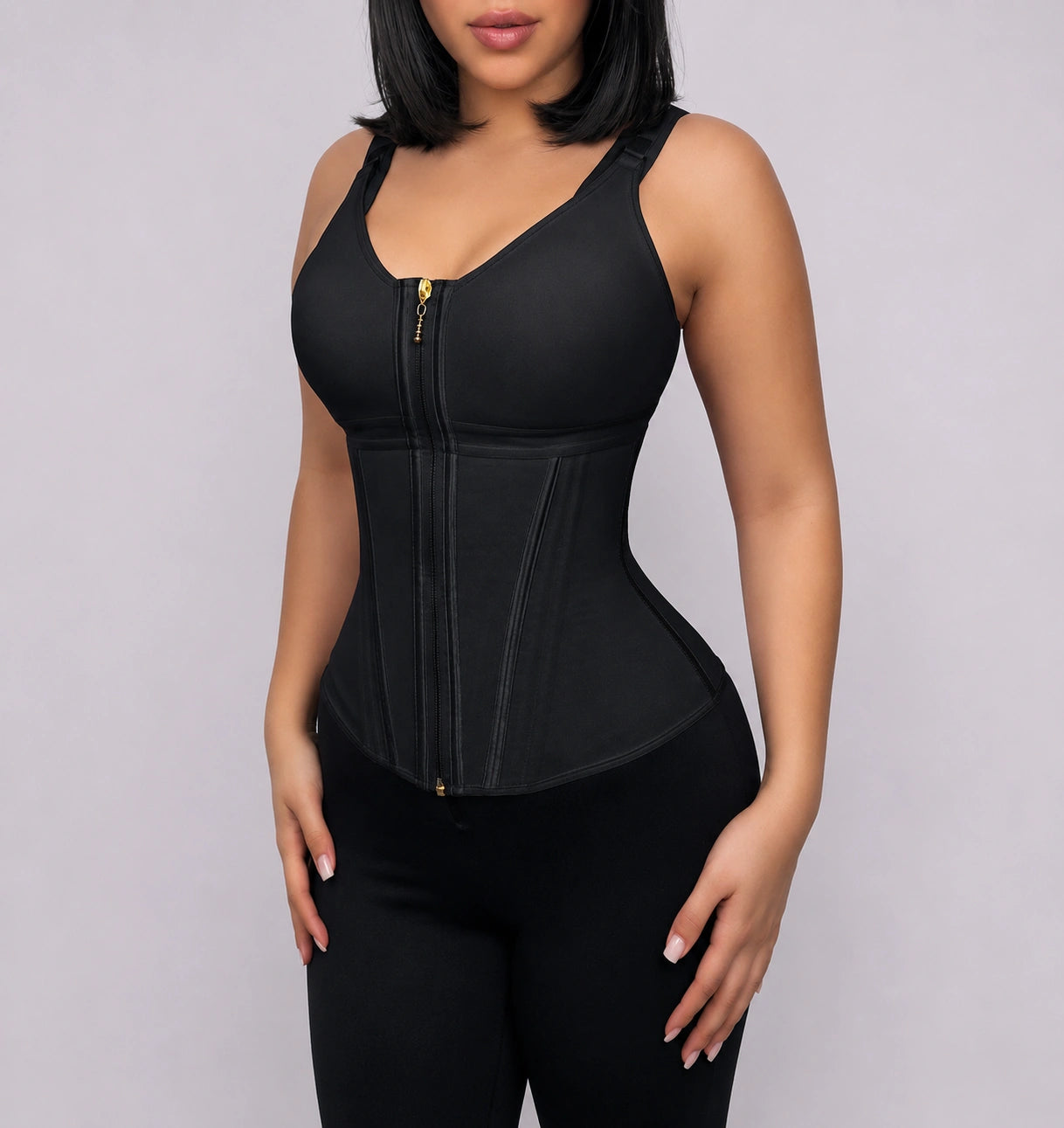 Woman wearing a black structured shapewear corset with adjustable shoulder straps, contoured waist panels, and a gold-tone front zipper.